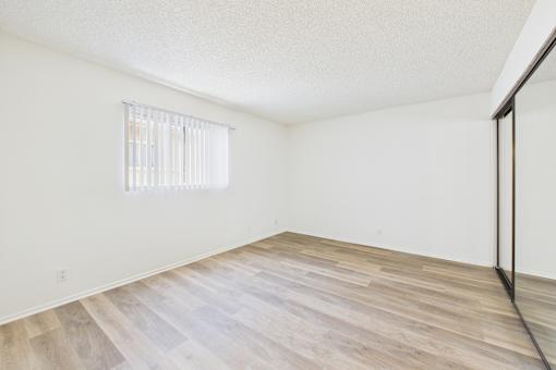 A room with wooden flooring and a window with blinds.