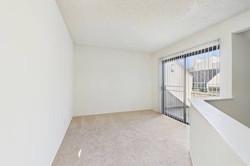 Empty room with a carpeted floor and a window with a view of a building outside.