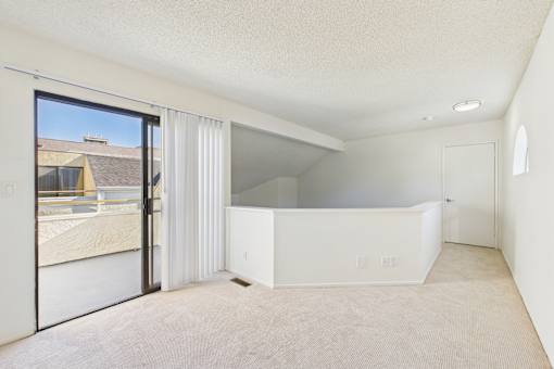 A large, empty room with a sliding glass door leading to a balcony.