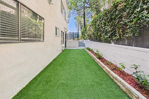 A narrow alley with a green artificial lawn and a white wall on the right.