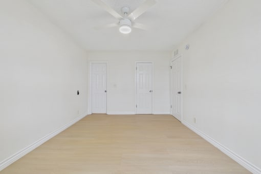 A room with a ceiling fan and three doors.