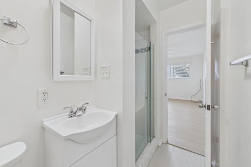 A white bathroom with a sink, mirror, and shower.