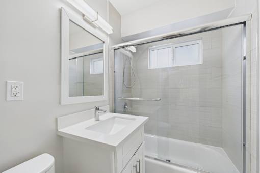 A white bathroom with a sink, mirror, and bathtub.