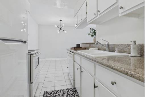 A kitchen with white cabinets and a black and white patterned rug on the floor.