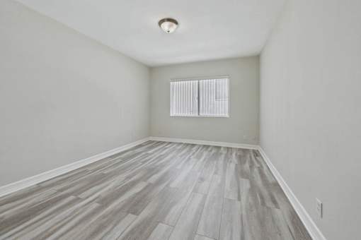 A room with wooden flooring and a window with blinds.