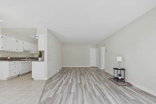 A spacious room with a kitchen area to the left and a wooden floor.