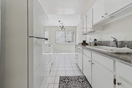 A kitchen with white cabinets and a black and white patterned rug.