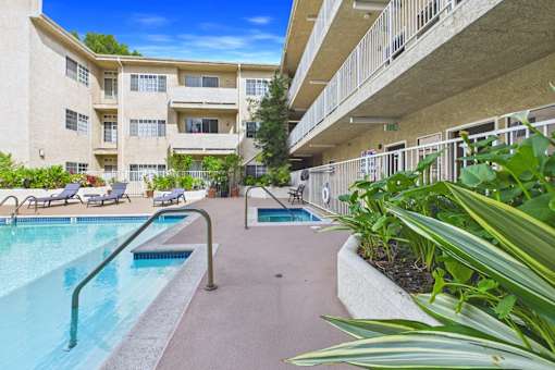A swimming pool is surrounded by a concrete walkway and a grassy area.