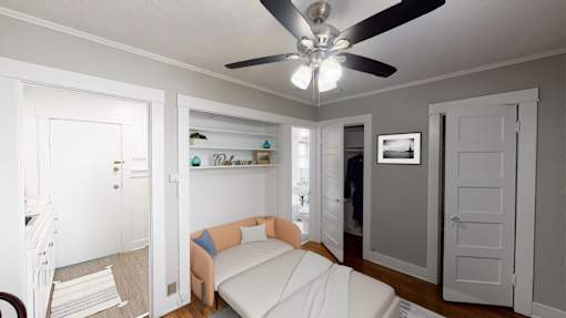 A white bedroom with a bed, a fan, and a shelf with decorations.