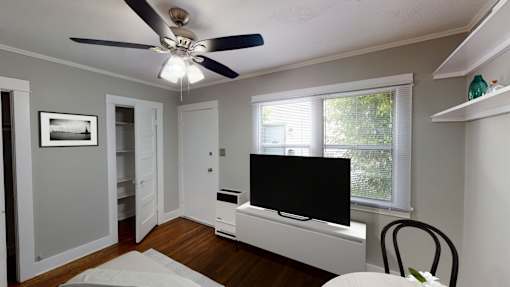 A room with a ceiling fan and a television on a cabinet.