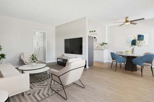A living room with a white couch, a white chair, a black chair, a white coffee table, a black coffee table, a white TV, a white cabinet, a white plant, a white ceiling fan, a white wall, a