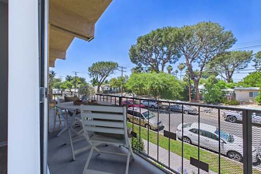 A balcony with a chair and a view of a parking lot.