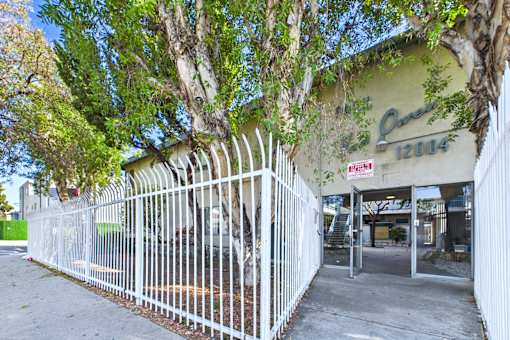 A white fence surrounds a building with a green sign that says Ques.