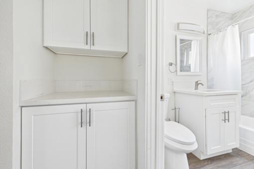 A white bathroom with a toilet, sink, and cabinets.