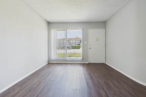 A room with a white door and a window with a view of a fence and a building outside.