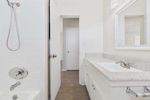 A white bathroom with a shower, sink and mirror.