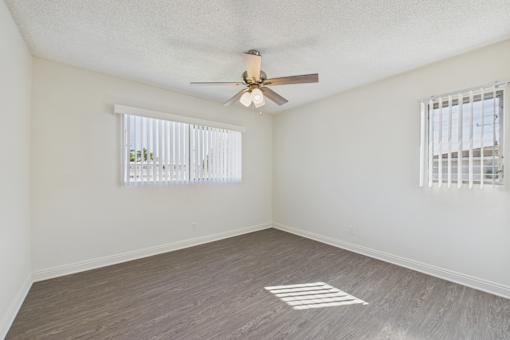 A room with a ceiling fan and two windows with blinds.