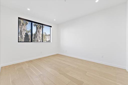 A room with wooden flooring and a window showing trees outside.