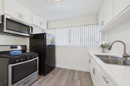 A black refrigerator sits in a kitchen with white cabinets and a stove.
