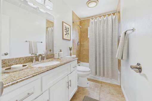 A bathroom with a sink, mirror, toilet, and shower.