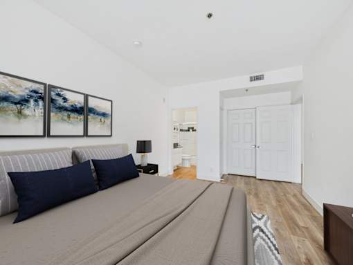 A bedroom with a bed, a painting, a lamp, and a door.
