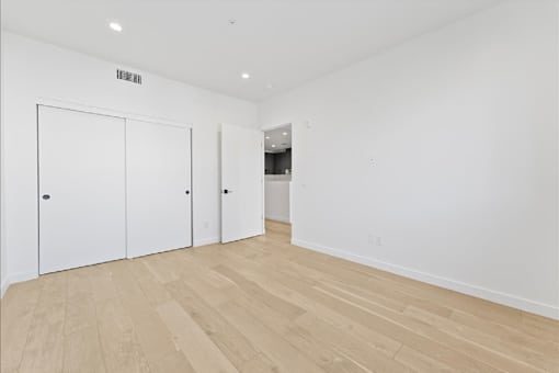 A room with white walls and wooden flooring with two white doors.