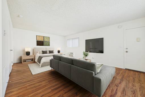 A grey couch is in the middle of a white room with a bed and a television.