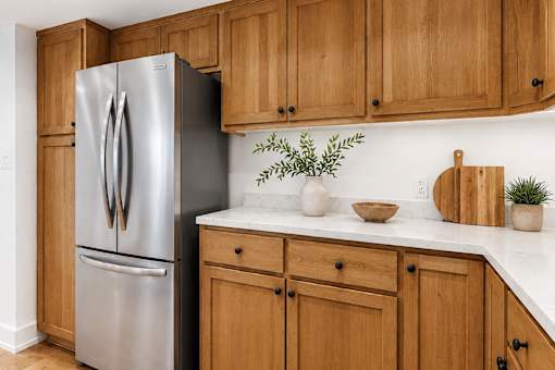 A stainless steel refrigerator stands next to wooden cabinets in a kitchen.