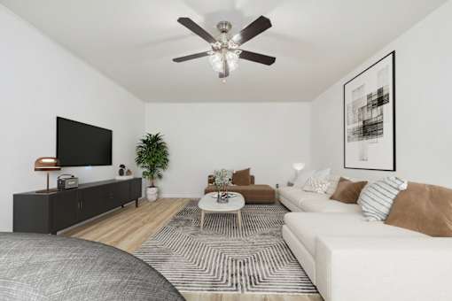 A living room with a white couch, a wooden floor, and a ceiling fan.
