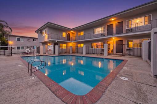 A swimming pool in front of a building with lights on.