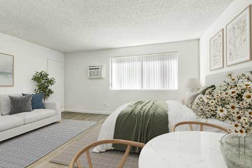 A living room with a white couch, a round wooden table, and a white bed with a green blanket.