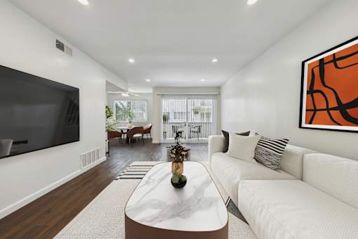A modern living room with a white sofa and a large TV on the wall.