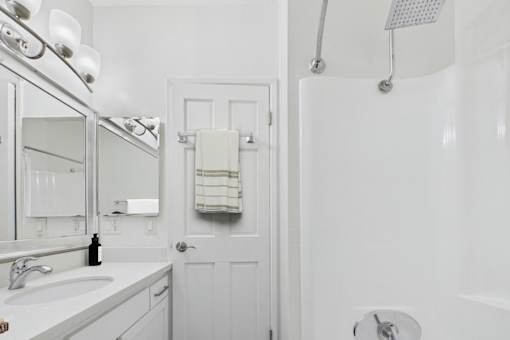 A white bathroom with a white tub and a white towel hanging on the door.