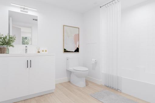 A white bathroom with a toilet, a cabinet, a plant, and a painting on the wall.