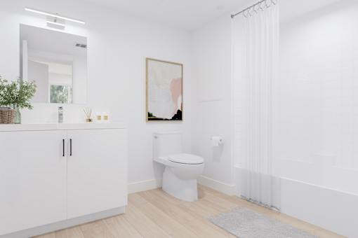 A white bathroom with a toilet, a cabinet, a plant, and a painting on the wall.