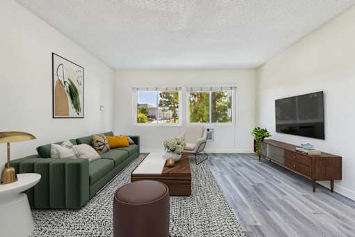 A living room with a green couch, a coffee table, a chair, a lamp, a plant, and a flat-screen TV mounted on the wall.