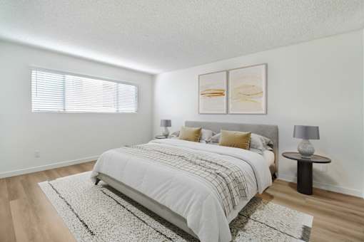 A bedroom with a large bed and a small table with a lamp on it.