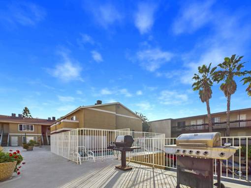 A sunny day at a residential complex with a barbecue grill in the foreground.