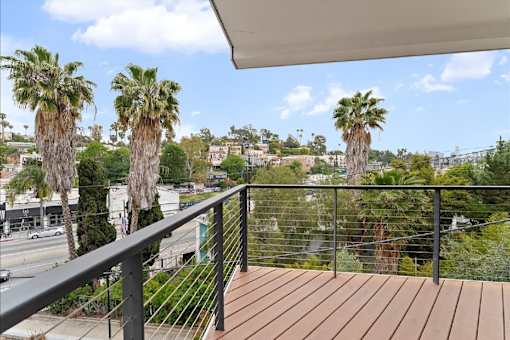 A balcony with a wooden floor and a metal railing with palm trees in the background.