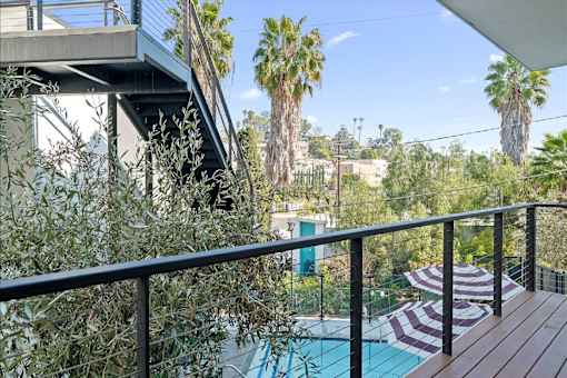 A pool with a striped umbrella and a balcony with a railing.