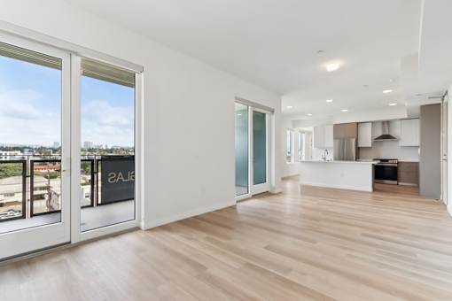 A spacious room with wooden flooring and a view of the city through the windows.