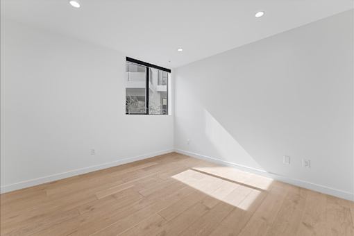 A room with wooden flooring and a window showing a building outside.