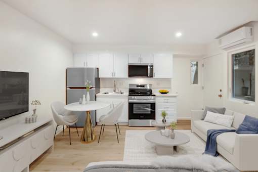 A modern kitchen with white cabinets and appliances, a dining table with chairs, and a living area with a couch.
