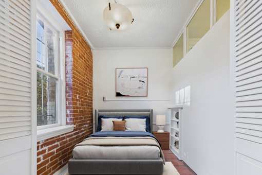 A bedroom with a brick wall and a bed with a blue headboard.