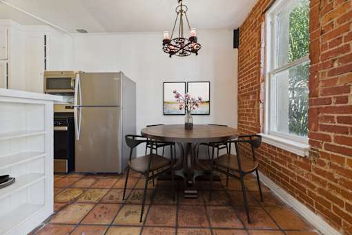 A kitchen with a refrigerator, a dining table with chairs, and a painting on the wall.