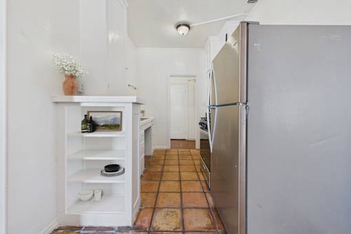 A kitchen with a white fridge and a white shelf with a vase of flowers on it.