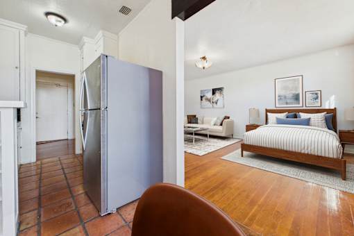 A kitchen with a refrigerator and a bedroom with a bed.