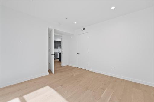 A room with a wooden floor and white walls with a doorway leading to another room.