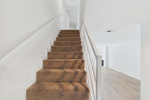 A staircase with a brown carpeted runner and white balusters.