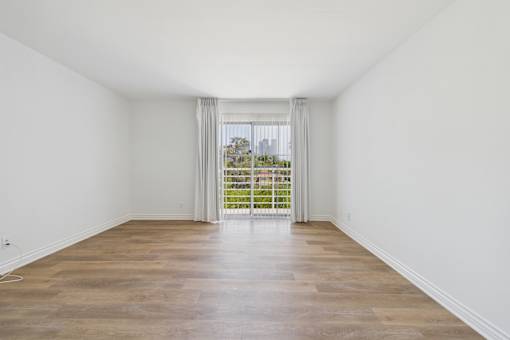A room with wooden floors and white walls leading to a balcony.